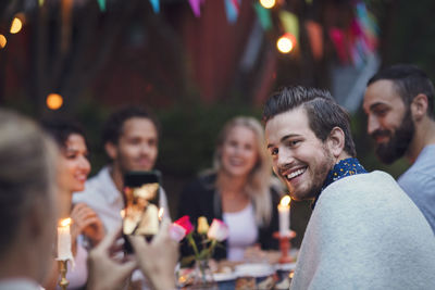 Woman photographing man while sitting with friends at garden party