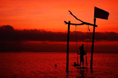 Silhouette people on swing over sea against sky during sunset