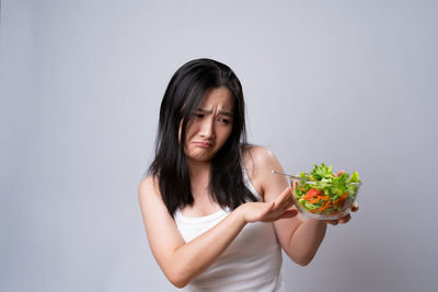 Portrait of young woman holding ice cream against white background