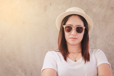 Portrait of young woman wearing sunglasses against wall