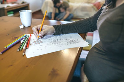 Woman drawing on paper with family in background at home
