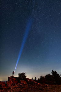 Person holding flashlight while standing on rock formation against star field