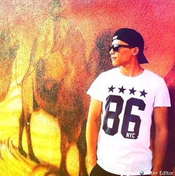 Young man looking away while standing against wall