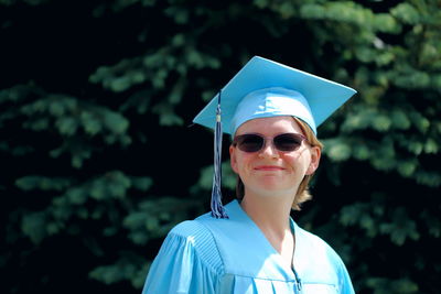 Smiling woman with mortarboard against trees