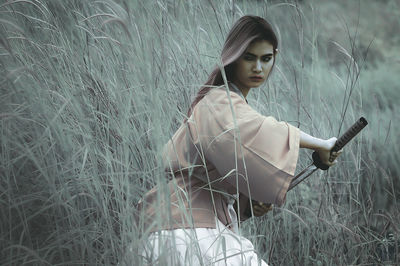 Young woman with sword amidst grassy field