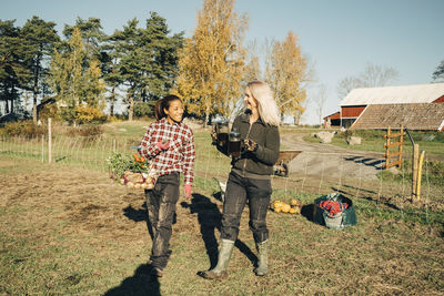 Smiling female farmers with vegetables and french press walking on field