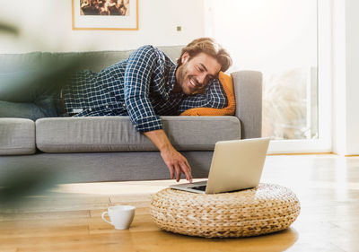Young man lying on the couch at home looking at laptop