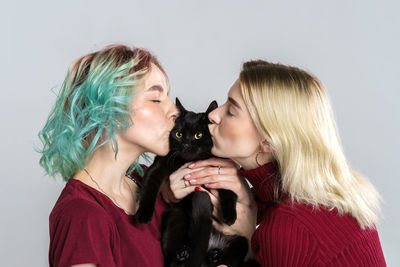 Portrait happy girls in casual clothes on light background, holding black cat