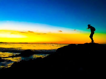 Silhouette man on rocks at beach against sky during sunset