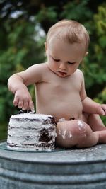 Portrait of cute baby boy in diaper sitting by layer cake looking down