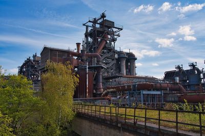 Metallic structure by factory against sky