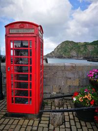 Red telephone booth by building against sky