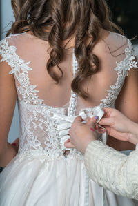 Cropped hands of woman dressing bride during wedding