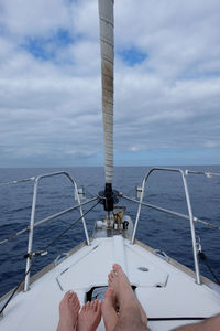 Low section of couple sailing on sea against sky