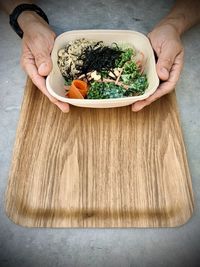 Cropped hands of man holding bowl with food on table