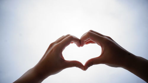 Close-up of cropped hands making heart shape against clear sky