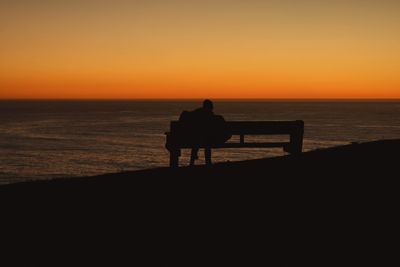 Silhouette man sitting on beach against clear sky during sunset