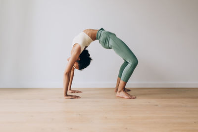 Yoga teacher practicing yoga position of bridge against white wall and wood floor with copy space