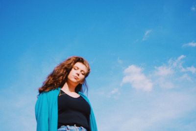 Low angle view of young woman standing against blue sky