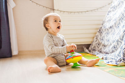 Cute boy playing with toy sitting on floor at home