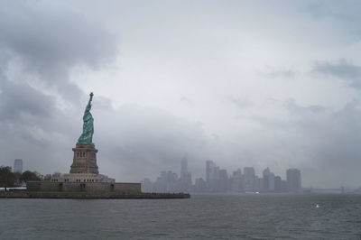 Statue of buildings in city against cloudy sky