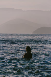 Man swimming in sea against sky during sunset