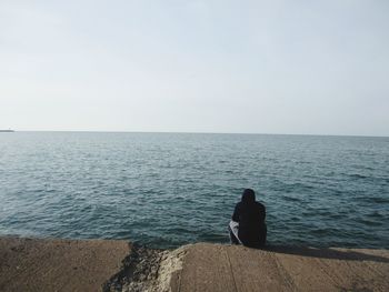 Rear view of man sitting on sea against clear sky