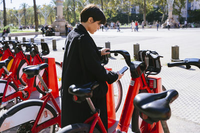 Woman renting bicycle through smart phone at parking station