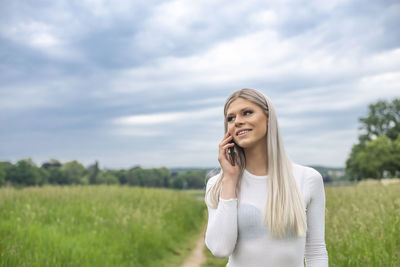 Portrait of smiling young woman standing on field against sky