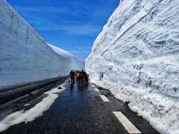 People walking on snowcapped mountain road against sky