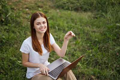 Portrait of young woman using mobile phone while sitting on field