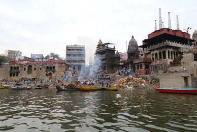 Boats in river amidst buildings in city against sky