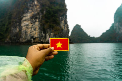 Cropped hand holding star shape label over sea against mountain