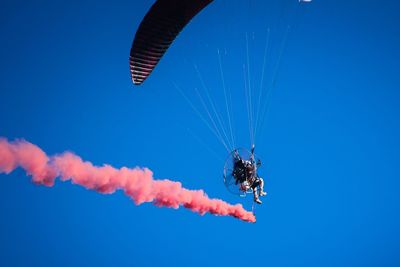 Low angle view of person paragliding against clear blue sky during sunny day