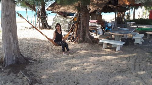 Full length portrait of woman on tree at beach