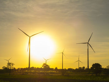 Wind turbines on field against sky during sunset