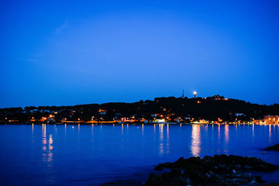 Illuminated city against clear blue sky at night