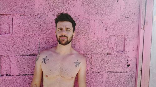 Portrait of shirtless young man with star shape tattoo standing against pink wall