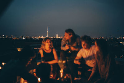 Friends enjoying on terrace against cityscape at dusk