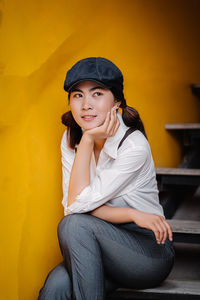 Portrait of smiling young woman sitting against yellow wall