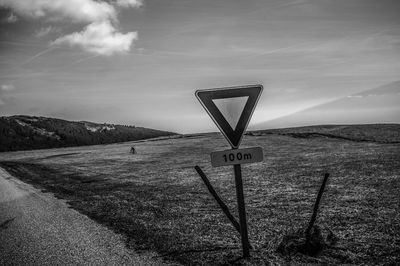 Road sign on field against sky