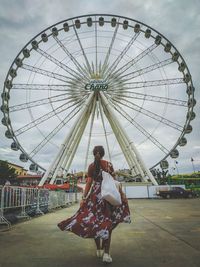 Rear view of people with ferris wheel against sky