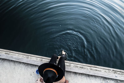 High angle view of woman in fedora hat sitting on pier by sea