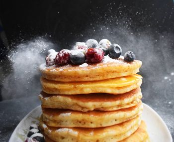 Close-up of pancakes stacked in plate against black background