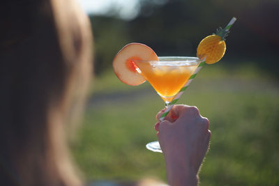 Woman holding orange peach cocktail in glass with ice cubes and straw