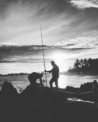 Silhouette men fishing at beach against sky
