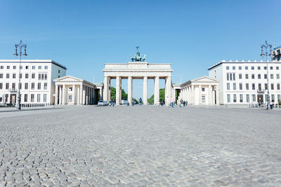 Brandenburg gate by street in city against blue sky