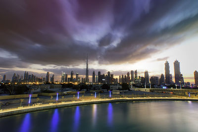 Illuminated city by river against sky