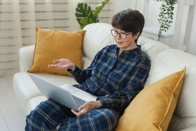 Young woman using laptop while sitting on sofa at home