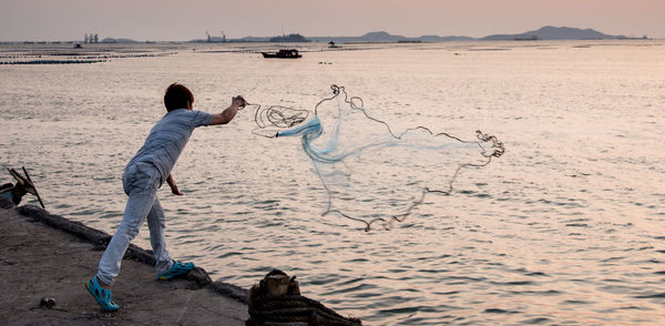 Fisherman throwing fishing net in sea during sunset